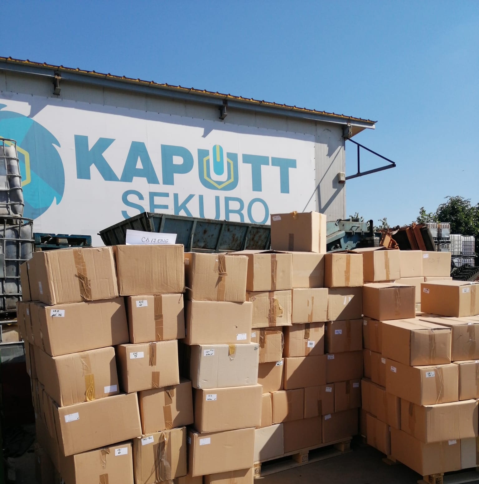 Grămezi de cutii de carton pregătite pentru distrugere securizată, în fața clădirii KAPUTT SEKURO